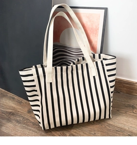 Detail of large striped canvas tote bag showing thick white straps on wooden floor