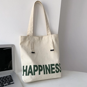 Détail d'un sac cabas en toile beige avec imprimé Happiness vert sur un bureau blanc
