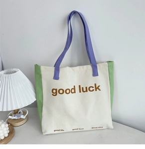 Detail of color-block canvas tote bag with good luck lettering and purple shoulder strap