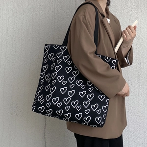 Detail of black canvas tote bag with white heart print worn over the shoulder