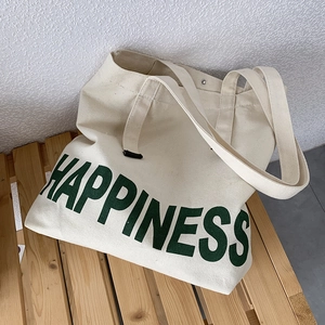 Détail d'un sac fourre-tout en toile beige avec texte HAPPINESS vert posé sur un banc en bois