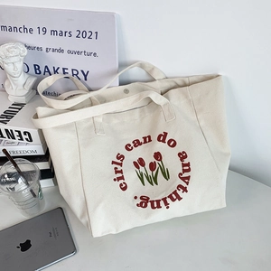 Detail of canvas tote bag with red tulips and Girls can do anything printed slogan