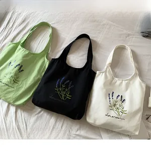 Close-up of three canvas tote bags in green, black and white with lavender embroidery