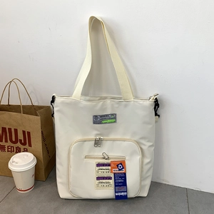 Detailansicht der cremeweißen Multi-Pocket-Tasche mit Boarding-Pass-Aufdruck und Anhängern