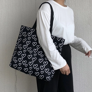 Detail of black canvas tote bag with heart print shown from a side view on a shoulder