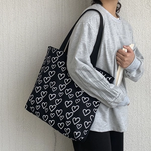 Detail of black canvas tote bag with white heart print worn over the shoulder by a model