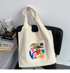 Close-up of white canvas tote bag with abstract floral print on a black leather chair