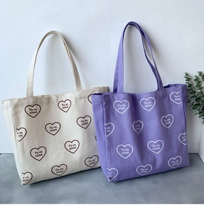 Détail de sacs fourre-tout en toile crème et violet avec imprimé cœur et poignées solides