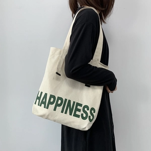 Détail du cabas en toile blanc cassé avec imprimé Happiness porté par un mannequin