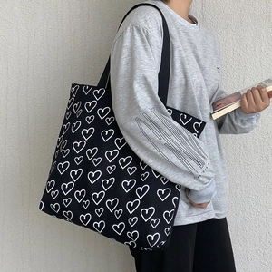Close-up of black canvas tote bag featuring white heart print and wide shoulder strap