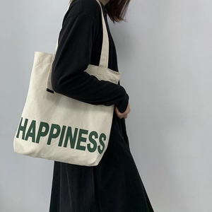 Vue latérale d'un sac cabas en toile blanche avec imprimé Happiness vert porté à l'épaule
