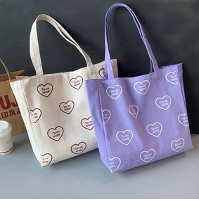 Détail de sacs fourre-tout en toile violet et crème avec motifs cœurs et lettrage français