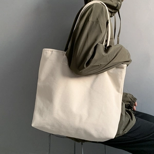 Side view of large off-white canvas tote bag worn over shoulder with casual outfit
