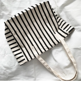 Flat lay of a striped canvas tote bag with cream handles on a white fabric background