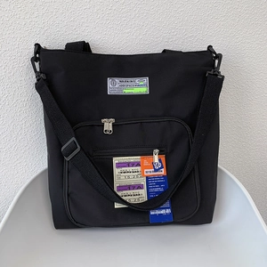 Detail der schwarzen Nylontasche mit Warning-Patch und Bordkarten-Grafikdruck für Damen