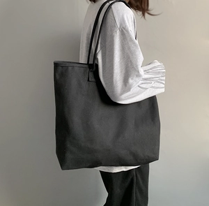 Detail of a large black canvas tote bag showing the spacious interior on a female model
