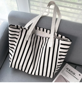 Close-up of black and white striped canvas tote bag with metal snap button on a sofa