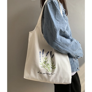 Detailed shot of white canvas tote bag with lavender print worn on woman's shoulder