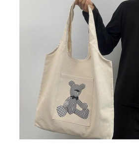 Detail of canvas tote bag featuring a beige pocket with a houndstooth bear pattern