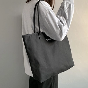 Detail of a large black canvas tote bag with white text print on a soft indoor background