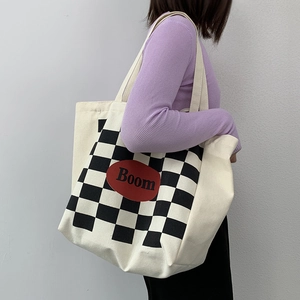 Detail of checkered canvas tote bag with red Boom patch shown worn by a model