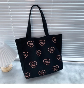 Détail du sac cabas en toile noire avec motifs de cœurs roses et texte Tu es aimé