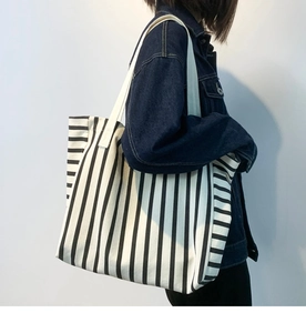 Side view of large black and white striped canvas tote bag worn by a model