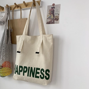 Détail d'un sac cabas en toile crème avec texte HAPPINESS vert et boucles noires élégantes