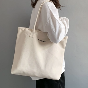Detail of a large off-white canvas tote bag worn by a model in a minimalist style