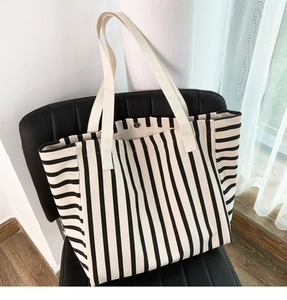 Detail of striped canvas tote bag with snap button and wide straps on leather chair
