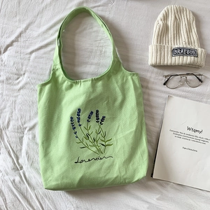 Light green canvas tote bag with lavender flower embroidery on a minimalist white surface