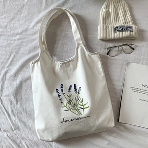Detailed flat lay of white canvas tote bag featuring lavender floral print and script text