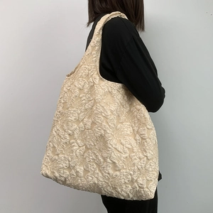 Détail de la broderie jacquard florale sur le cabas crème porté à l'épaule du modèle