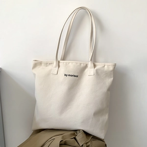 Detail of a minimalist cream canvas tote bag with black logo and long shoulder strap