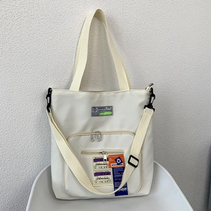 Detail der cremeweißen Nylon-Tragetasche mit Bordkarten-Etiketten und Reißverschlussfächern