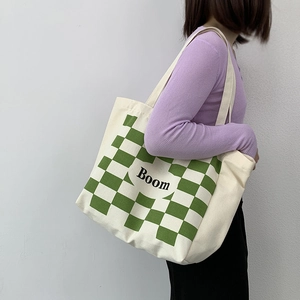 Close-up of green checkerboard canvas tote bag featuring Boom print on shoulder