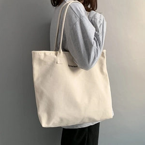 Close-up of high-density cream canvas tote bag with black print shown on model's shoulder