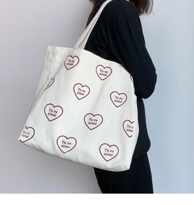 Détail d'un sac cabas en toile blanche avec motifs de cœurs rouges et texte