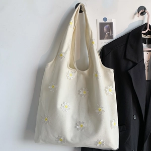Close-up of white canvas tote bag featuring delicate daisy embroidery and floral texture