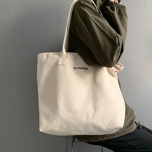 Detail of a large off-white canvas tote bag featuring by morisot print on model shoulder