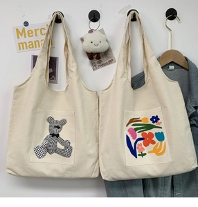 Detail view of canvas tote bags with bear and floral prints and convenient front pocket