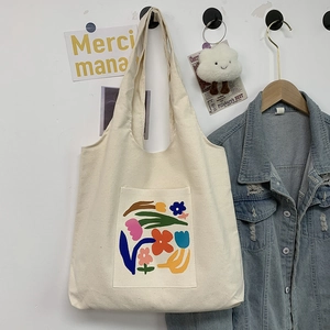 Close-up of a white canvas tote bag with a colorful floral pocket and denim jacket