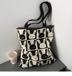 Detail of canvas tote bag with black and white rabbit checkerboard pattern and shoulder straps