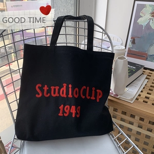 Detail of a black canvas tote bag with red Studio Clip 1949 embroidery on an iron chair