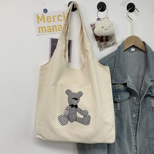 White canvas tote bag with houndstooth teddy bear pocket on minimalist wall background