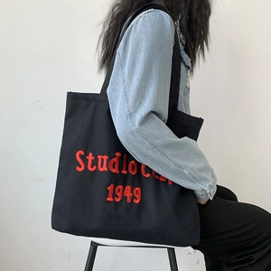 Detail of red Studioccc 1949 embroidery on black canvas tote bag with shoulder strap