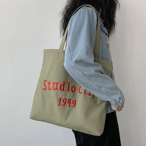 Close-up of olive green canvas tote bag featuring red Studio Clip 1949 embroidery