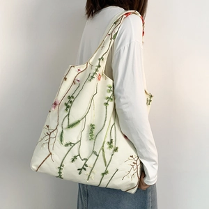 Detailed close-up of intricate plant embroidery on a cream canvas tote bag