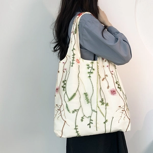 Detailed close-up of floral embroidery and green vine patterns on canvas tote bag