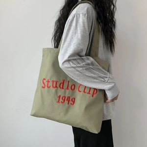Close-up of olive green canvas tote bag with red Studio CLIP 1949 embroidery detail